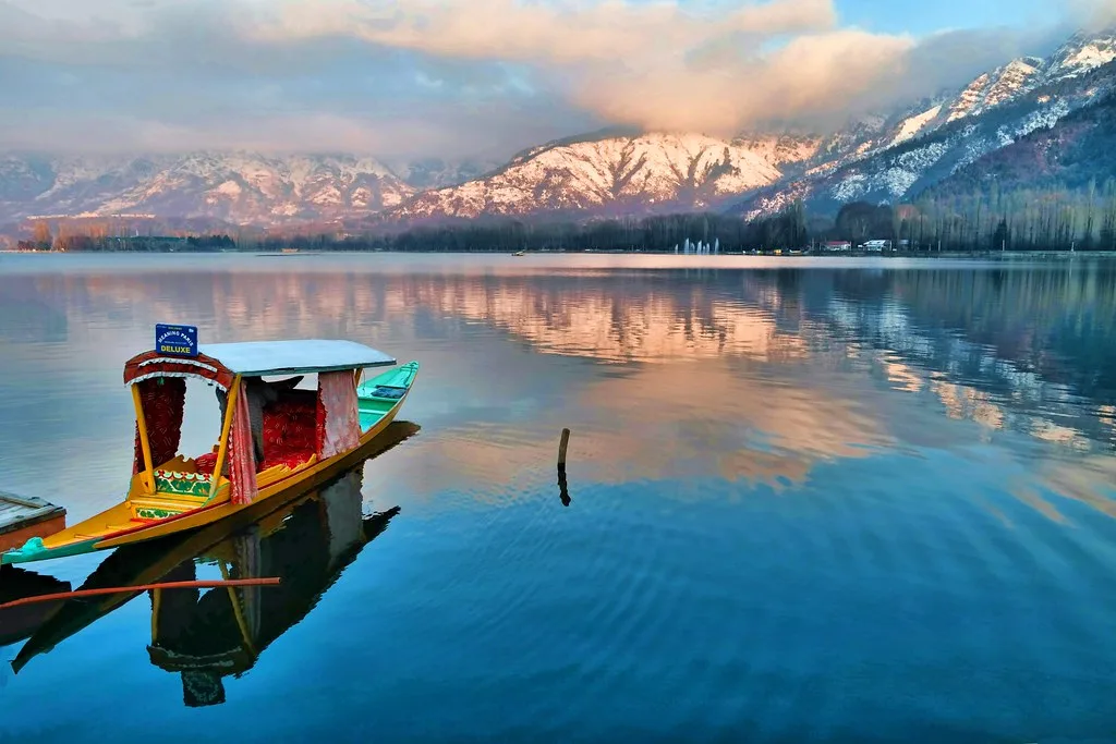 Shikara boat floating on Dal Lake Srinagar with snow-capped Himalayan mountains in the background, showcasing the serene beauty of Srinagar, Kashmir | By JKV Travel